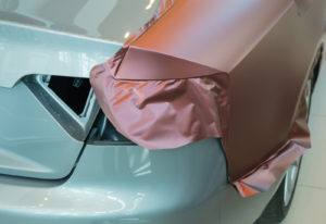 Mahogany-colored, adhesive-backed vinyl being wrapped on a car