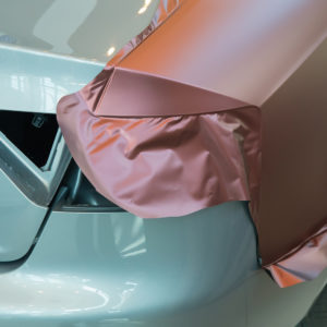 Mahogany-colored, adhesive-backed vinyl being wrapped on a car