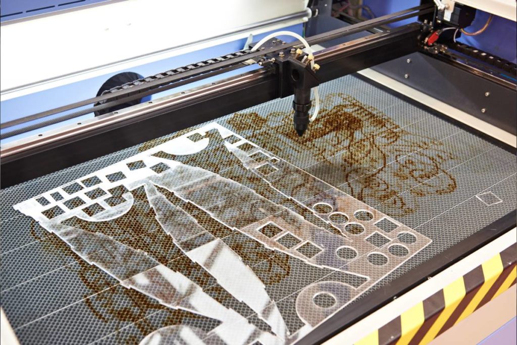 a clear plastic sheet with pieces cut out on a laser cutting table